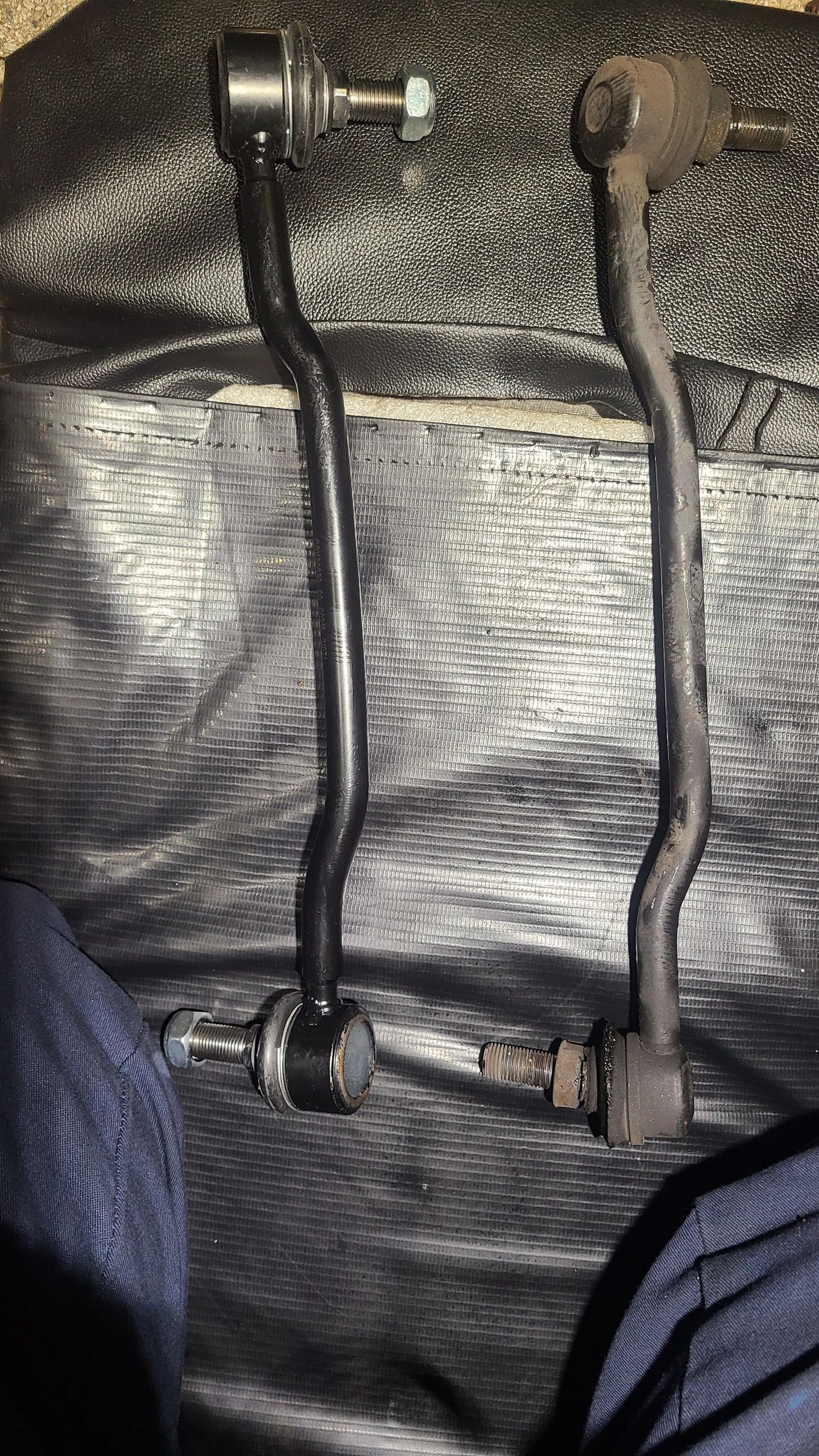 Tech On The Way — bent worn tie-rod end beside new straight replacement part laid out on a floor mat for comparison